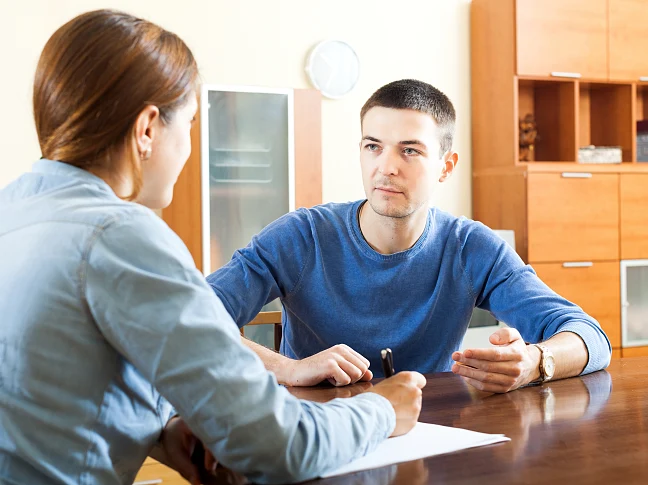 Ansicht eines Beratungsgespräches Sozialarbeiterin mit Fragebogen bei Mann am Tisch zu Hause